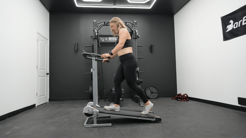 A woman walks at a slight incline on a manual treadmill.