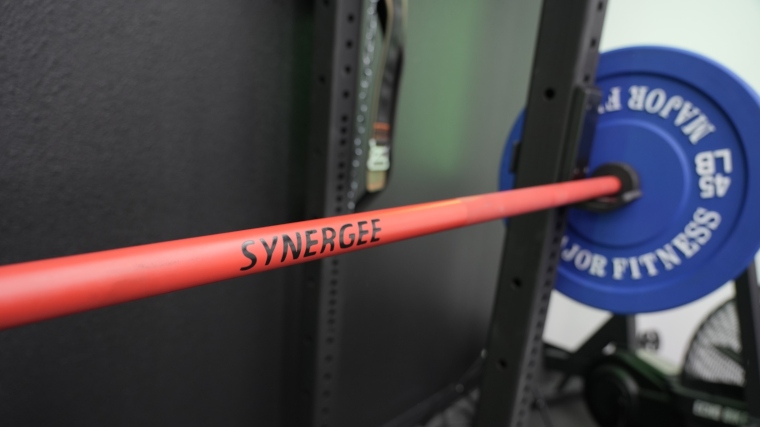 A Synergee Games Cerakote Barbell rests on the rack with the logo on display