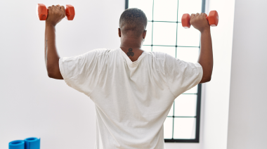 A young person lifts dumbbells while facing away from the camera.