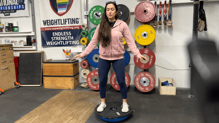 A woman balances. on both feet ontop of the REP Fitness Balance Ball Trainer.