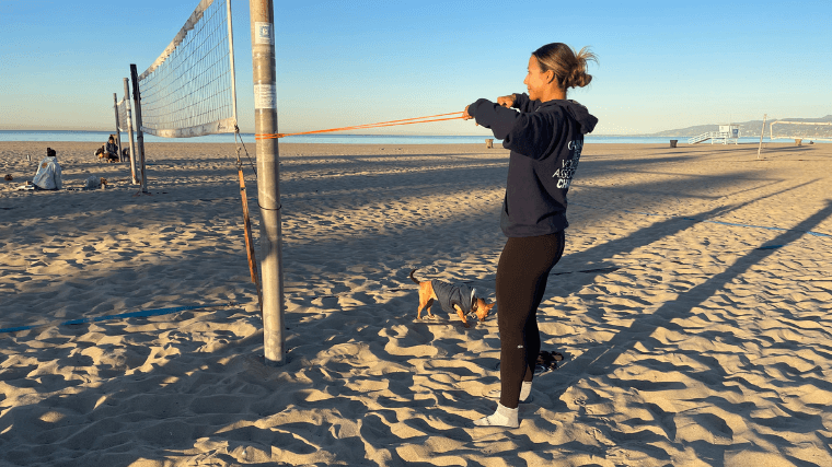 A woman warms up her shoulders before playing beach volleyball.