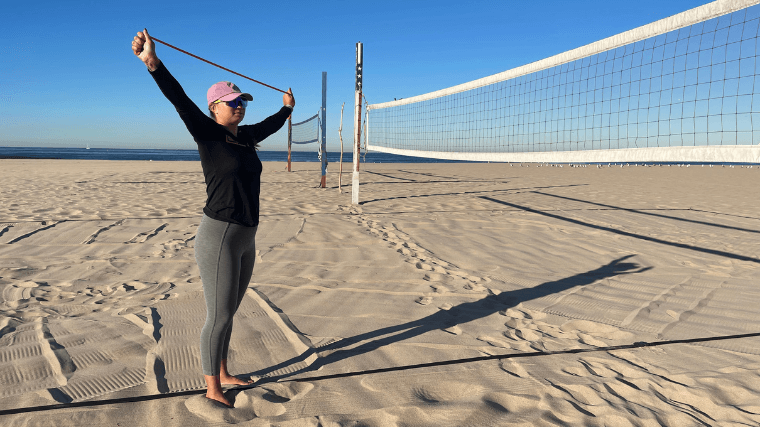 A woman warms up her shoulders before playing beach volleyball.