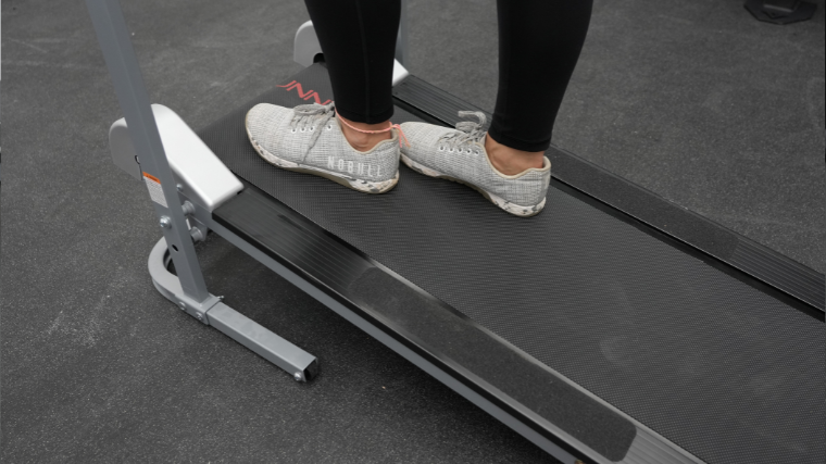 A close up look of a woman standing on a manual treadmill in NOBULL shoes.