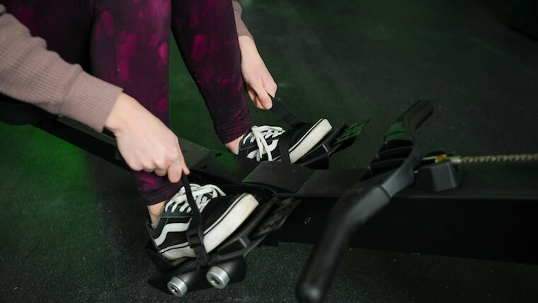 Our tester strapping their feet in the foot pedals on the Vulcan Scull Rower