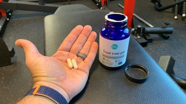 A man holding two capsules of Ora Organics Daily Essential Probiotic and Prebiotic in a gym