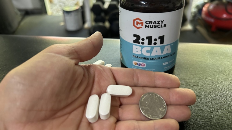 Our tester holds some Crazy Muscle BCAA tablets with a coin for size comparison.