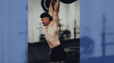 Justin Medeiros lifts a barbell over his head.
