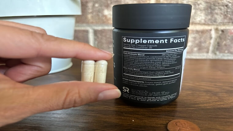 Our tester holding two Sports Research Probiotic capsules while reading the supplement facts